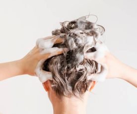 A girl washes her hair with shampoo on a white background, back view.