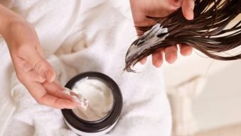 Person applying hair mask to wet hair, close-up of hands and hair.