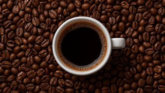 White cup of black coffee on coffee beans background, top view.
