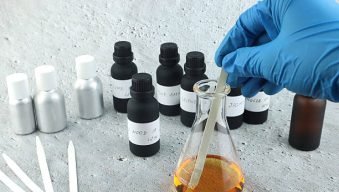 chemical beaker , flask is on white table with blotting paper , fragrance bottle and essential oil bottle are used to blend the nice scent for making perfume and candle by perfumer in the laboratory of home fragrant factory